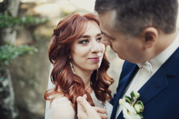 Bride looks in groom's eyes with love standing on the rocks