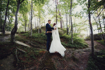 Bride and groom hug each other tender standing in the bright forest