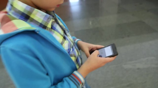 Closeup of child walking in terminal of airport and using smartphone. Age of little boy is 9 years old. Real time full hd video footage.