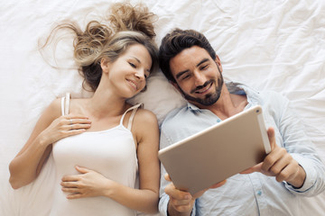 Attractive couple using tablet in bedroom. Top view.