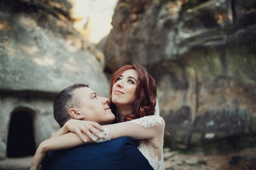 Fototapeta premium Bride looks up in the sky hugging groom before the rocks