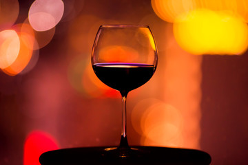Silhouette of glass with wine. Night city light at background.