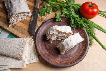 Two pieces of pita bread or lavash roll with cottage cheese or curd, chicken, tomatoes and herbs - dill, onion, parsley on brown clay plate..