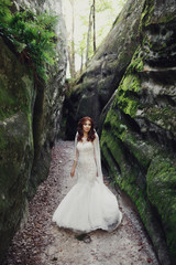 Stunning bride with red hair walks between green rocks