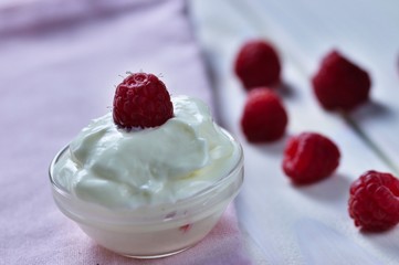 Glass bowl of yogurt decorated by raspberry, set on pink tea towel