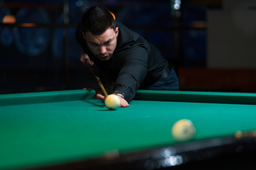 Young man aiming to take snooker shot in dark club