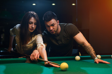 Young romantic couple playing snooker in club