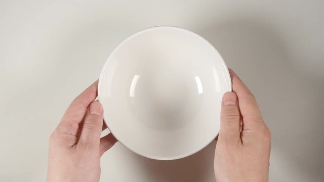 TOP VIEW: Human hands puts a white soup bowl on a white table