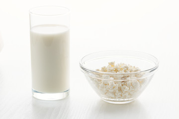 Milk in a glass, cottage cheese in a bowl, on a white table, in a high key, close-up with place for text