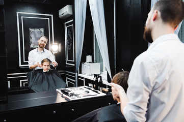 Young handsome barber making haircut of cute boy in barbershop