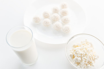 Milk in a glass, candy Raffaello cottage cheese in a bowl in the background, on a white table, in a high key