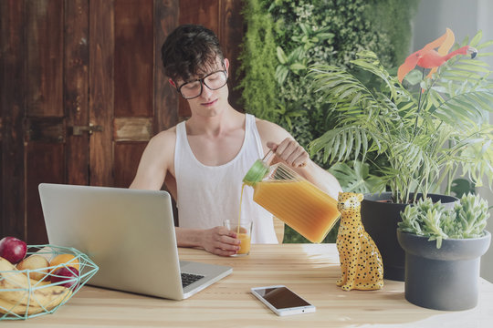 Young man pouring orange juice into glass at home