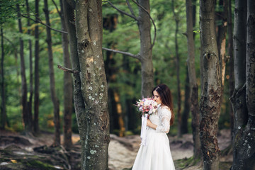 Obraz na płótnie Canvas The charming bride stands near trees