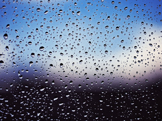 Water drops at the window glass at the blue sky with white clouds background