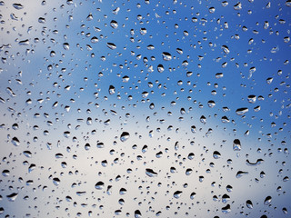 Water drops at the window glass at the blue sky with the clouds background