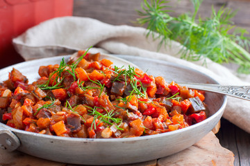 Stewed vegetables (eggplant, peppers, tomatoes) in a frying pan on a wooden table, selective focus, horizontal
