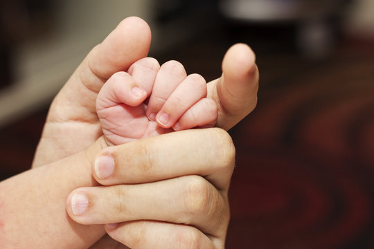 Cute fingers of newborn hold by his mother. A concept of care and love.
