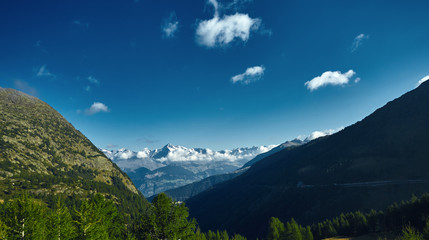Snow capped mountains under deep blue sky. View from the valley through the forest and trees