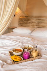 Obraz na płótnie Canvas Healthy Raw Fruit Breakfast in Bed. Color Smoothie on Wicker Tray on White Sheet.