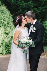 Tender kiss of bride and groom standing in green park