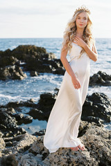 Lovely blond bride in white silk wedding dress posing near the sea