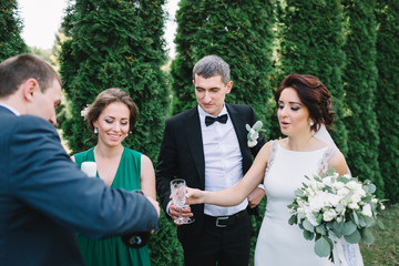 Happy wedding couple and friends drink champagne in green park