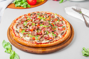 Selective focus close up Delicious Meat Pizza with bacon and sausages on the wooden board on the kitchen table with different bright ingredients