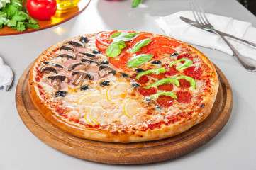 Fresh Italian Four Seasons Pizza (Pizza Quattro Stagioni) on the wooden board on the kitchen table with different bright ingredients. Selective focus