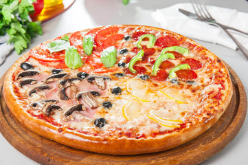 Fresh Italian Four Seasons Pizza (Pizza Quattro Stagioni) on the wooden board on the kitchen table with different bright ingredients. Selective focus