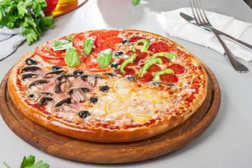 Fresh Italian Four Seasons Pizza (Pizza Quattro Stagioni) on the wooden board on the kitchen table with different bright ingredients. Selective focus