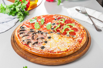 Fresh Italian Four Seasons Pizza (Pizza Quattro Stagioni) on the wooden board on the kitchen table with different bright ingredients. Selective focus