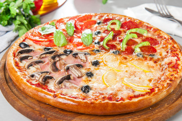 Fresh Italian Four Seasons Pizza (Pizza Quattro Stagioni) on the wooden board on the kitchen table with different bright ingredients. Selective focus
