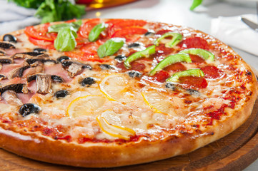 Fresh Italian Four Seasons Pizza (Pizza Quattro Stagioni) on the wooden board on the kitchen table with different bright ingredients. Selective focus