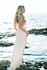 Lovely blond bride in white silk wedding dress posing near the sea