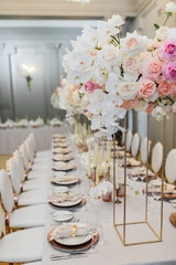 Tall square vase with pink and beige flowers stands on the dinner table