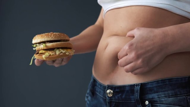 Overweight woman measure girth of her belly, against hamburger. The concept of fast food, overeating, poisoning