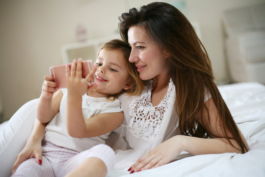 Smiling mother with daughter using smart phone on bed.