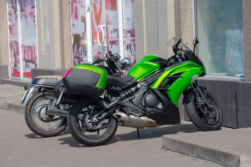 Green motorcycle parked on the sidewalk. Transport