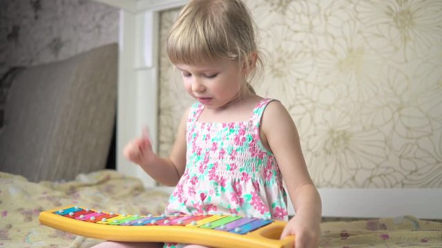 A little girl plays on a child's xylophone and sings