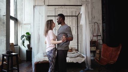 Multiethnic couple dancing in pajamas. African male and Caucasian female look happy, laughing and smiling, holding hands