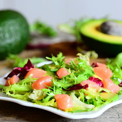 Salmon, avocado and lettuce salad on a plate. Diet salad with slices of smoked salmon, fresh avocado and lettuce leaves mix. Avocado fruit and half on a wooden table. Closeup 