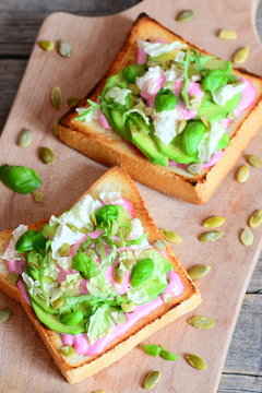 Sliced avocado, pumpkin seeds, lettuce, basil and beetroot sauce on a bread toast. Homemade open sandwiches on a wooden board and rustic wooden table. Diet and healthy toast meal. Vertical photo