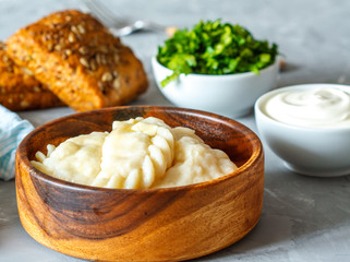 Cooked eastern european dumplings, vareniki with sour cream with parsley on gray background.