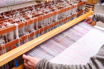 Close up hands of woman weaving pink and white pattern on loom