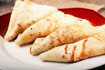 Homemade wheat crepes or pancakes with strawberry jam or marmalade stacked on a plate on a wooden rustic table
