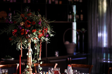 Fototapeta na wymiar Tall golden vase with bouquet of cranberries, red flowers and greenery stands on the table