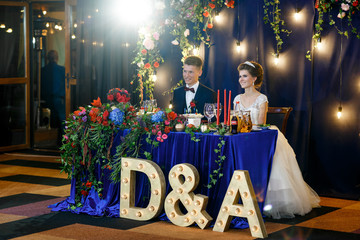 Letters D&A with lamps stand before dinner table covered with blue velvet cloth
