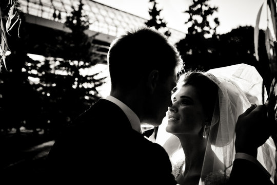 Black and white picture of groom kissing bride while he holds her veil up