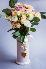 White vase with beige roses stands on grey background