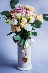 White vase with beige roses stands on grey background